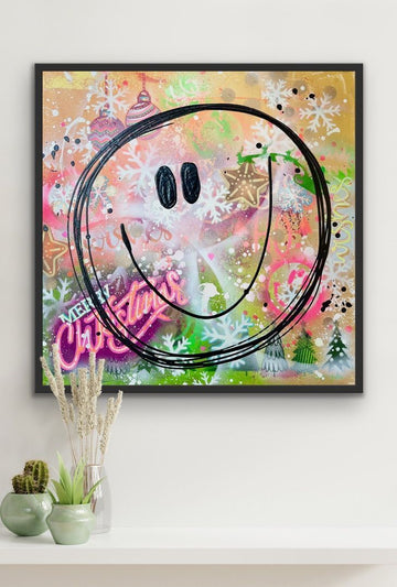 Einrichtungsbeispiel: Das bunte Pop-Art Weihnachtsbild 'Christmas Smile' in einem schwarzen Rahmen an einer weißen Wand. Darunter stehen kleine, grüne Kakteen auf einem weißen Sideboard.
