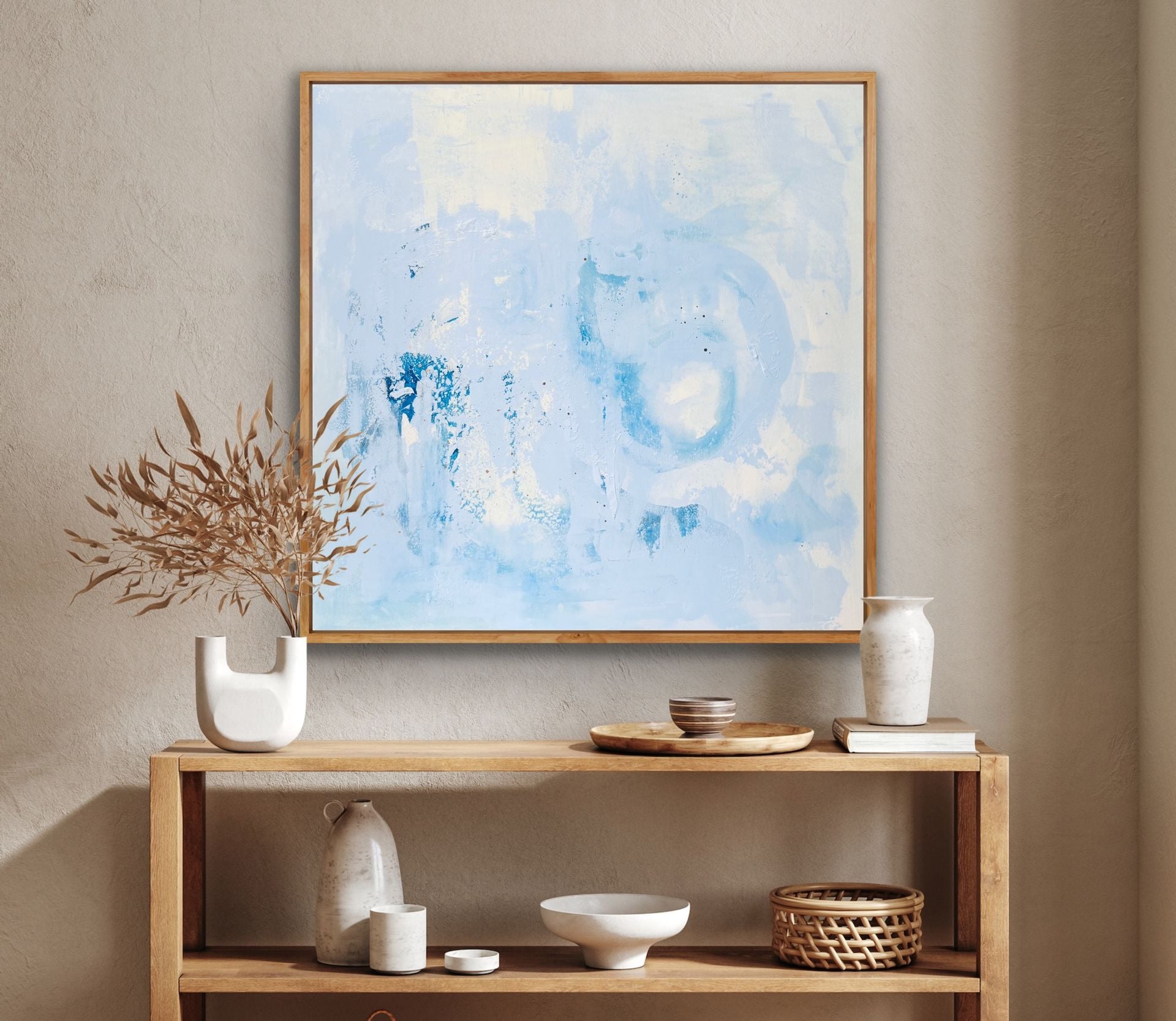 Einrichtungsbeispiel im Japandi-Stil: Das hellblaue Gemälde hängt in einem Holzrahmen über einem Holz-Sideboard, das mit Keramikvasen, einer Holzschale und Trockenblumen dekoriert ist.