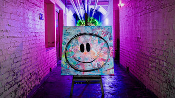 Inszenierung wie in einer Galerie: Das bunte Gemälde 'Big Smile' steht auf einer dunklen Holzstaffelei mitten in einem langen, alten Backsteingang, der komplett mit pinkem und lila Neonlicht ausgeleuchtet ist