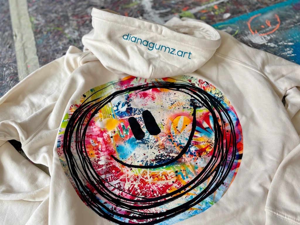 Ein Bio-Baumwoll-Hoodie mit einem farbenfrohen, abstrakten Smiley-Kunstwerk-Print auf der Brust, entworfen von der Kieler Künstlerin Diana Gumz.