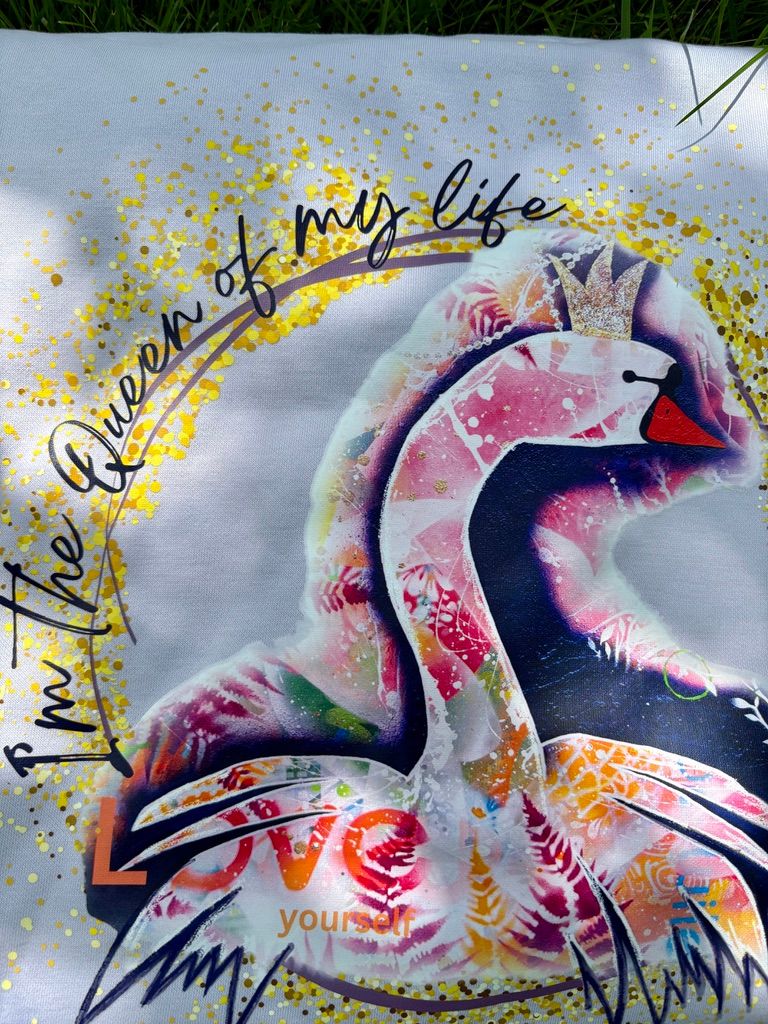 Detailaufnahme des großen, bunten Schwanen-Kunstprints auf dem Rücken des fliederfarbenen Hoodies im Sonnenlicht. Das Motiv zeigt einen Schwan mit Krone und die Schriftzüge 'I'm the Queen of my life' und 'LOVE yourself', umgeben von funkelnden goldenen Glitzer-Details.