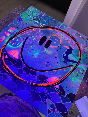 Nahaufnahme des Pop-Art Gemäldes 'Küsten Smile' unter Schwarzlicht (UV-Licht). Der Smiley, die Segelboote, Fische und 'Moin'-Texte leuchten in spektakulären, fluoreszierenden Neon-Farben.