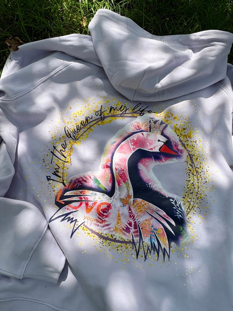 Fliederfarbender Kapuzenpullover. Auf dem Rücken ist ein großer, bunter Kunst-Print eines Schwans mit Krone zu sehen. Darum steht in goldener Schrift 'I'm the Queen of my life' und 'LOVE yourself'
