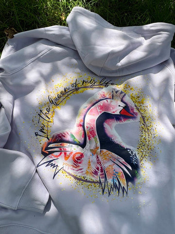 Fliederfarbender Kapuzenpullover. Auf dem Rücken ist ein großer, bunter Kunst-Print eines Schwans mit Krone zu sehen. Darum steht in goldener Schrift 'I'm the Queen of my life' und 'LOVE yourself'